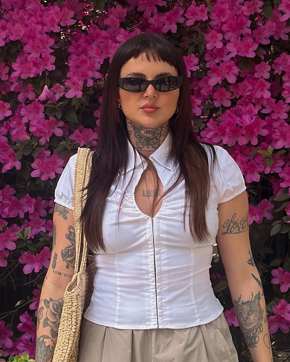 Sharon Pucinelli de óculos, diante de um arbusto florido